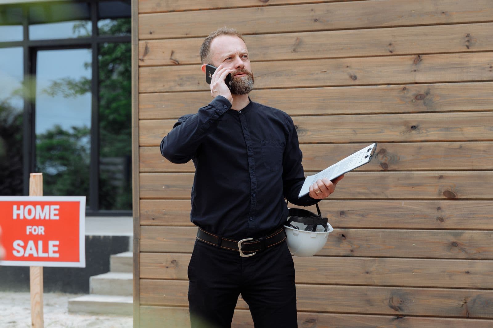 A real estate agent on the phone beside a home-for-sale sign